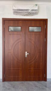 Bộ cửa composite hai cánh vân gỗ nâu, kết hợp ô kính phía trên và họa tiết huỳnh đối xứng tại công trình Hai Bà Trưng.