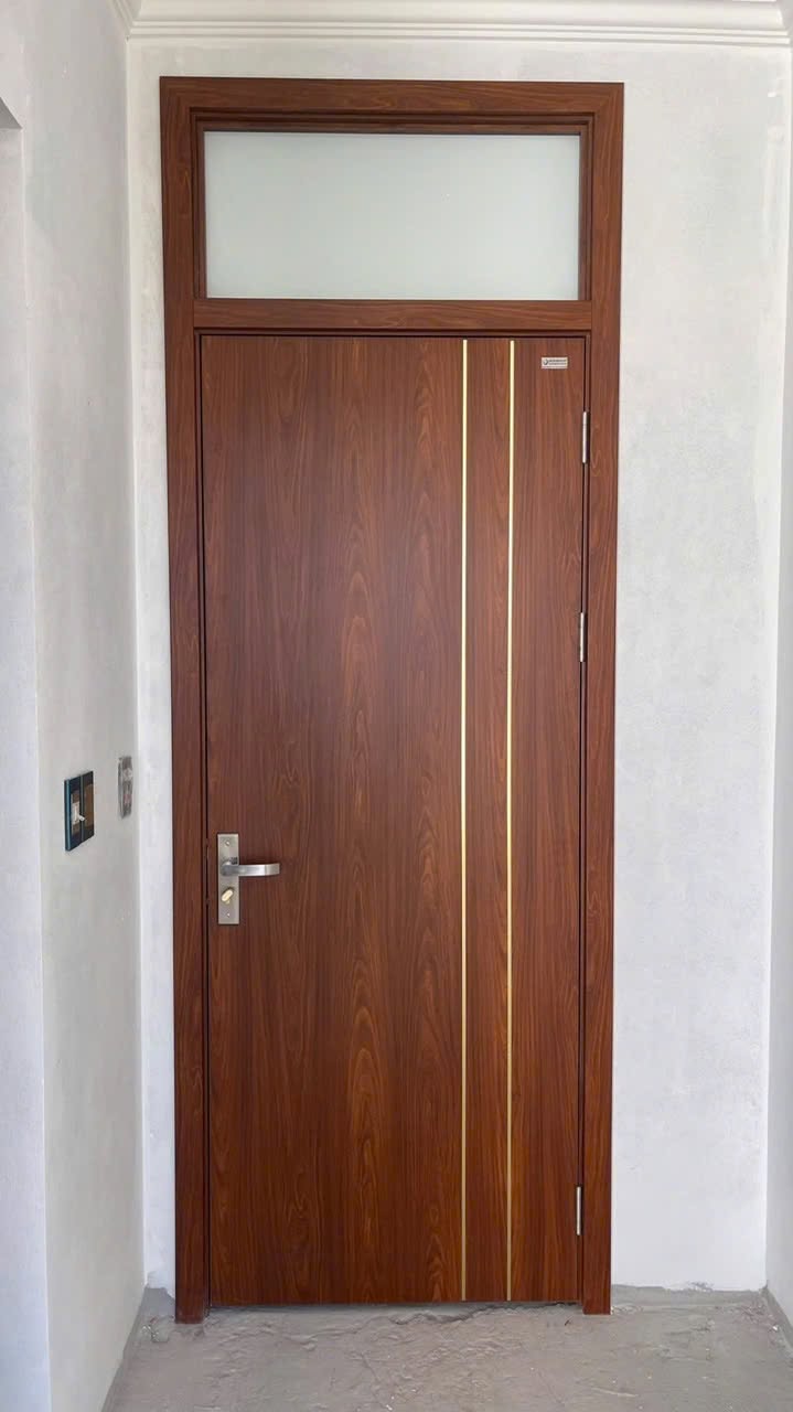 Cửa composite thông phòng vân gỗ nâu có hai đường chỉ dọc và ô kính phía trên tại Hai Bà Trưng