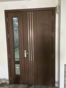 Cửa composite hai cánh lệch vân gỗ nâu, kết hợp ô kính đứng và các đường chỉ trang trí tại công trình Lạc Long Quân, Tây Hồ.