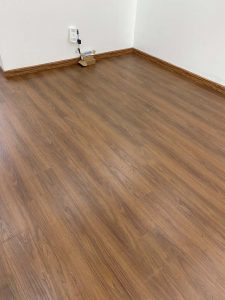 Mặt sàn Hobi H682 sau hoàn thiện trong phòng, kết hợp cùng tường trắng và phào chân tường màu gỗ